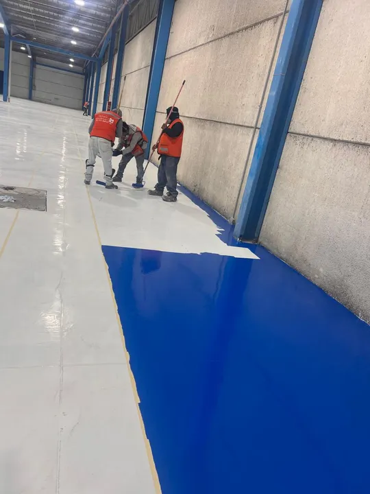 Aplicación de recubrimiento epóxico azul con rodillo junto a un área ya terminada en blanco.