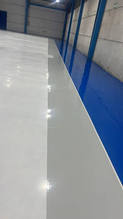 Piso epóxico terminado en gris y azul a lo largo del muro de una nave.