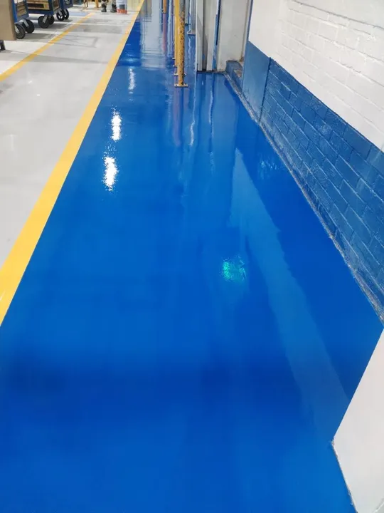 Pasillo de piso epóxico azul con acabado brillante junto a muro y columnas.