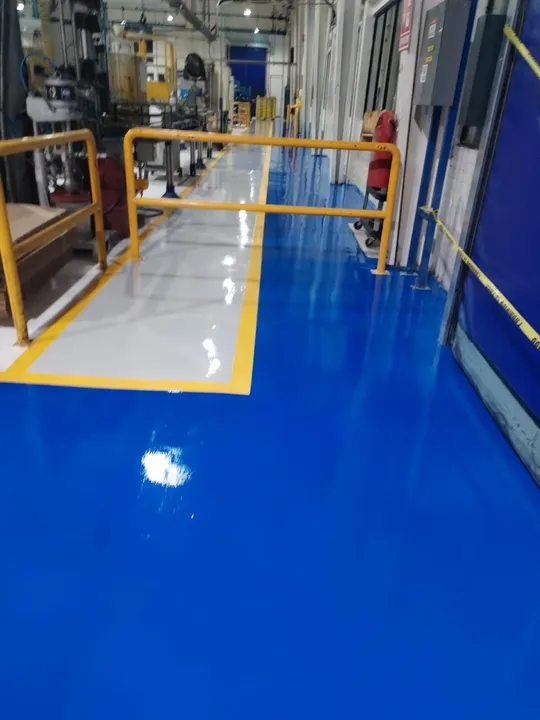 Piso epóxico azul en una línea de producción, con pasillo peatonal gris delimitado en amarillo.