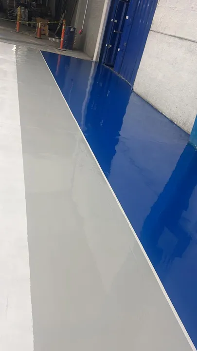 Pasillo con piso epóxico gris y franja azul brillante en una planta.